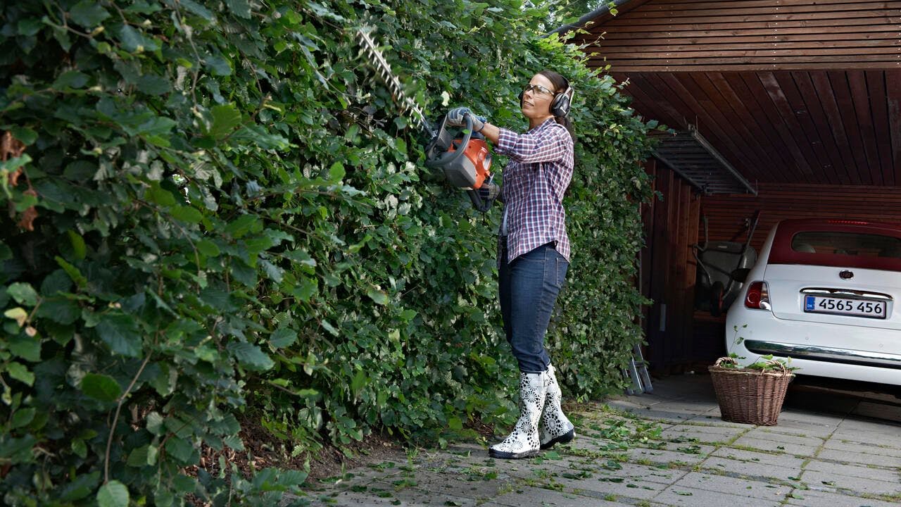 woman trimming hedges in driveway